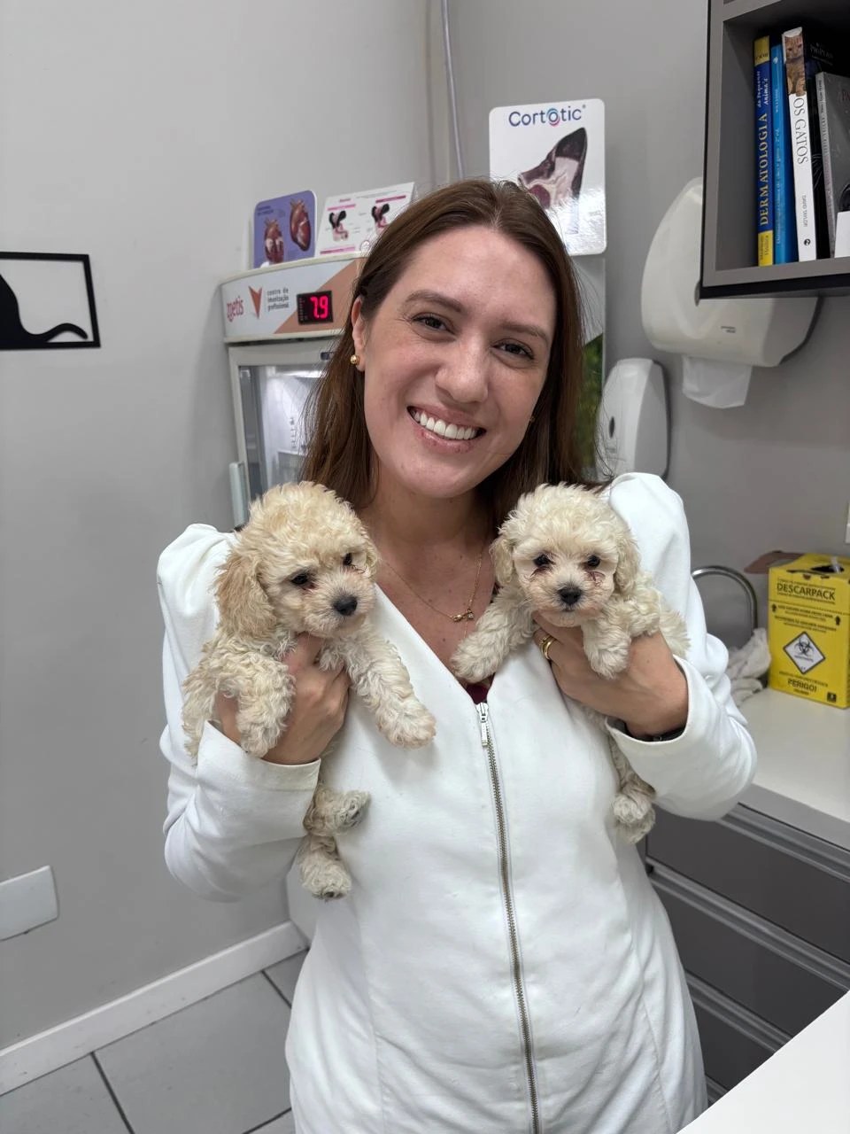 Dra. Juliana Ribeiro Felix, médica-veterinária responsável técnica da Interpet, sorrindo com dois filhotes de poodle no consultório